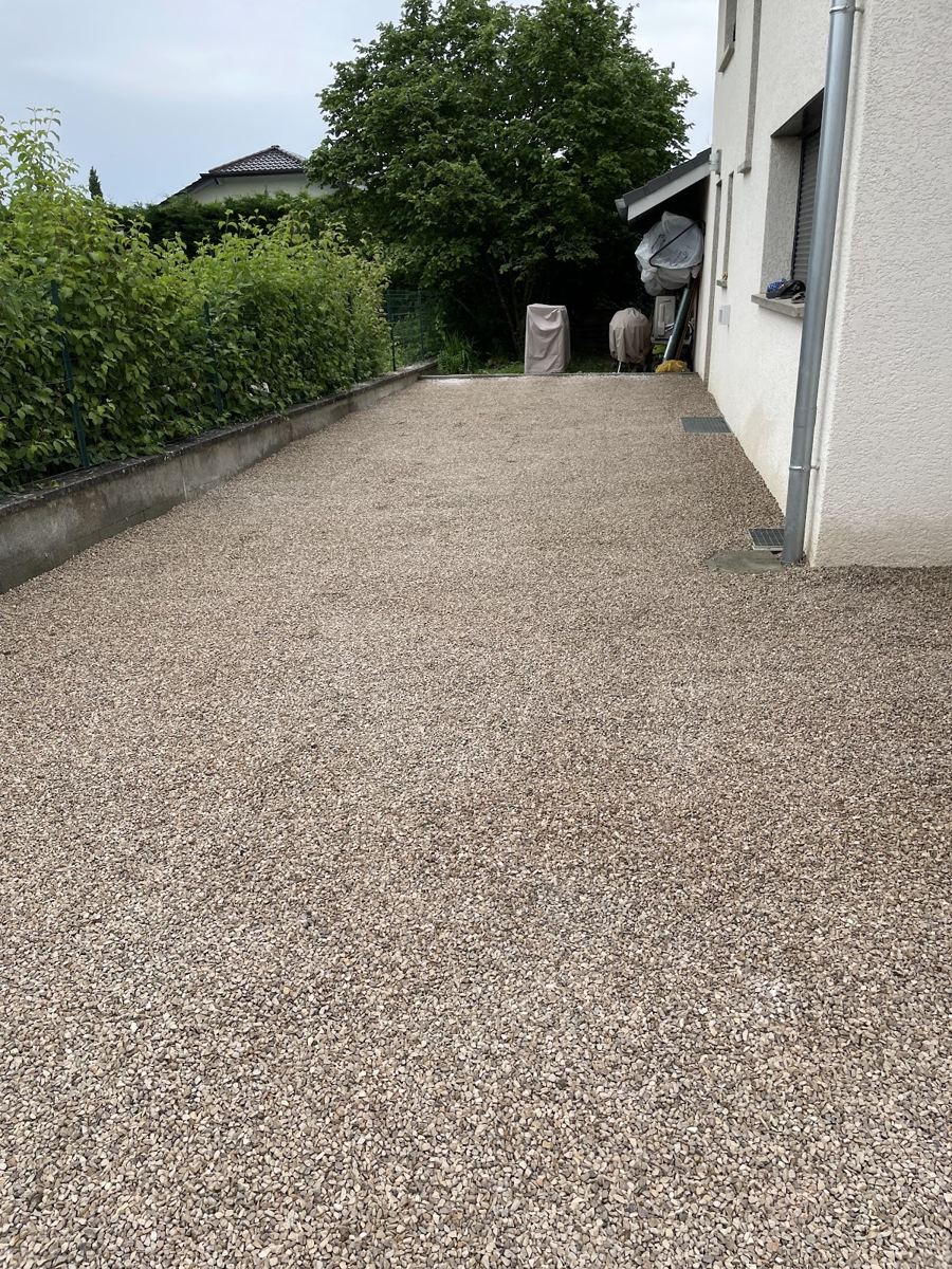 Allée d'entrée en gravier entre une haie et une maison