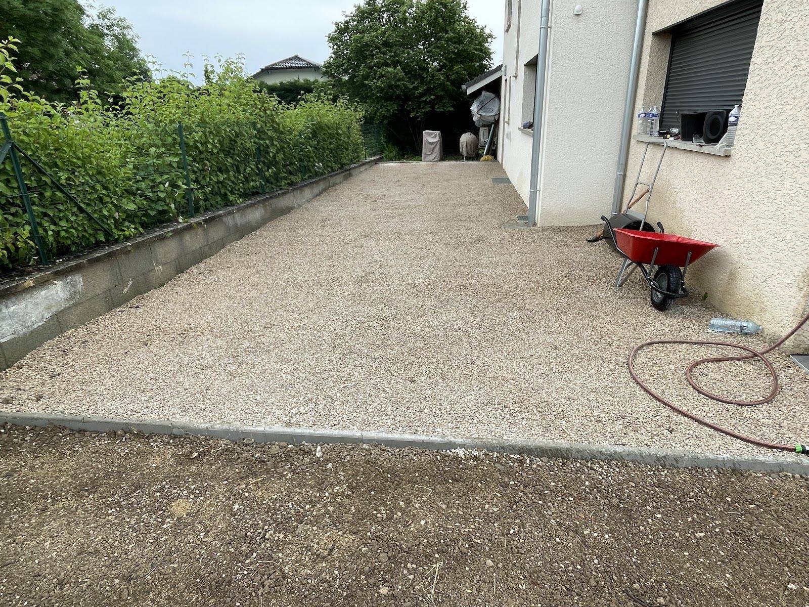 Allée en gravier bordurée le long d'une maison, haie à gauche